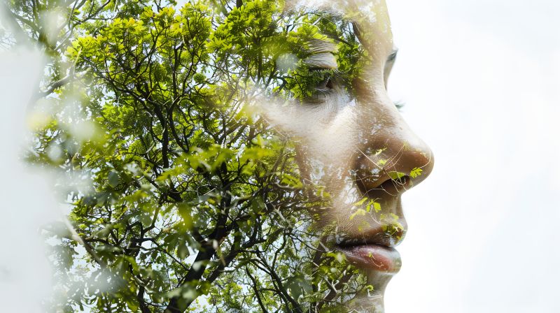 Doppelte Belichtung eines seitlichen Gesichtsporträts einer jungen Frau mit geschlossenen Augen kombiniert mit einem Bild von grünen Baumzweigen und Blättern.